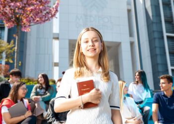 Medipol Üniversitesi önünde elinde kitap tutarak gülümseyen kız öğrenci.