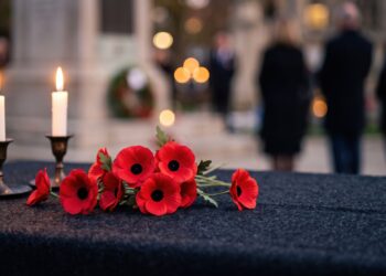 Siyah örtü üzerinde iki yanık mum ve kırmızı anma çiçekleri.