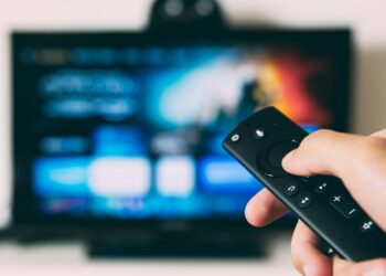 Televizyon izlerken elinde kumanda tutan bir kişinin elinin yakın plan görüntüsü.