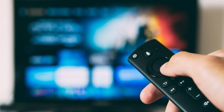 Televizyon izlerken elinde kumanda tutan bir kişinin elinin yakın plan görüntüsü.