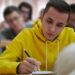 Sarı kapüşonlu genç bir öğrenci sınıfta ders çalışıyor ve yazı yazıyor.