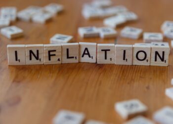 Ahşap masa üzerinde 'inflation' yazan Scrabble harf taşları yer alıyor.