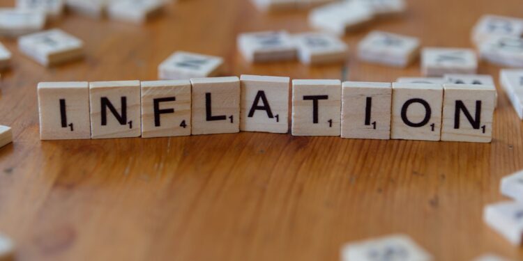 Ahşap masa üzerinde 'inflation' yazan Scrabble harf taşları yer alıyor.