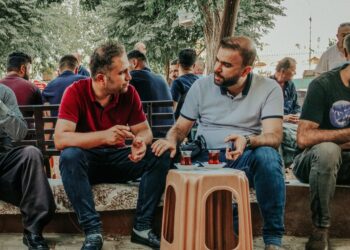 Açık havada plastik tabure etrafında oturup çay içen erkekler.