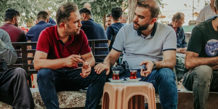 Açık havada plastik tabure etrafında oturup çay içen erkekler.