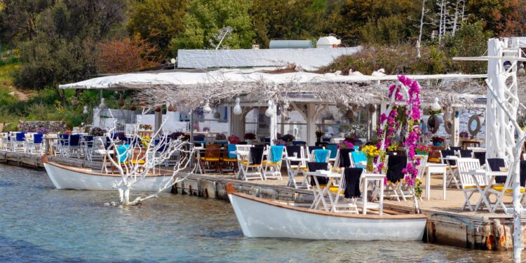 Deniz kenarındaki şık bir restoranın iskelesinde beyaz masalar ve sandalyeler.