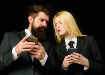 Siyah takım elbiseli bir erkek ve kadın ellerindeki akıllı telefonlara bakıyorlar.