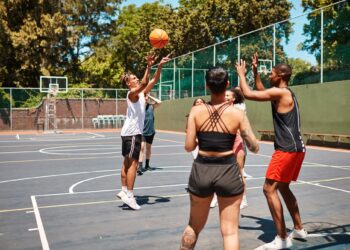 Açık havada basketbol sahasında top sürerek oynayan bir grup genç.