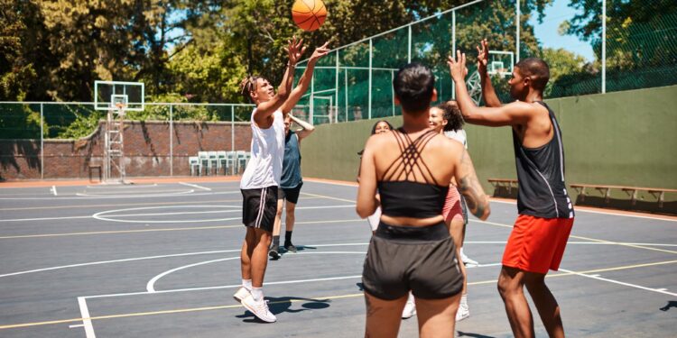 Açık havada basketbol sahasında top sürerek oynayan bir grup genç.