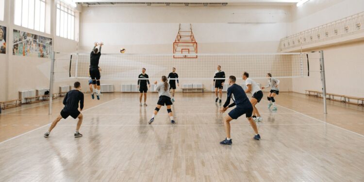 Kapalı salonda voleybol maçı yapan sporcular file önünde mücadele ediyor.