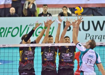 File önünde ellerini yukarı kaldırmış voleybol blok yapan sporcular.