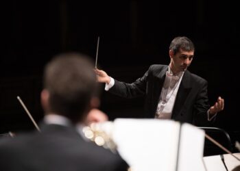 Siyah ceketli orkestra şefi orkestrayı yönetiyor.