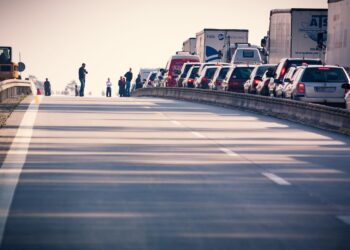Otoyolda trafikte duran araçlar ve yol kenarında bekleyen insanlar.
