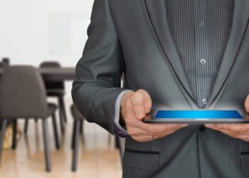 Takım elbiseli bir adam ellerinde ışıklı tablet bilgisayar tutuyor.