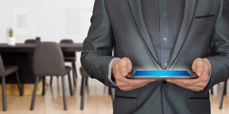 Takım elbiseli bir adam ellerinde ışıklı tablet bilgisayar tutuyor.