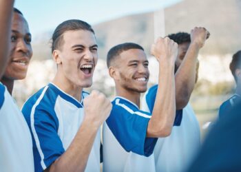 Mavi beyaz formalı futbolcular ellerini yumruk yapıp sevinç çığlığı atıyor