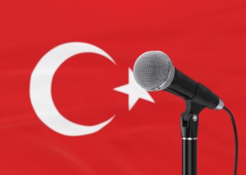 Kırmızı Türk bayrağı önünde siyah mikrofon ve mikrofon standı duruyor.