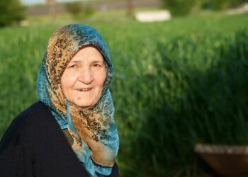 Açık havada yeşillikler arasında duran başörtülü yaşlı bir Türk kadını.