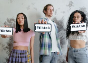 Üç genç elinde #tiktok yazılı akıllı telefonlar tutarak poz veriyor.