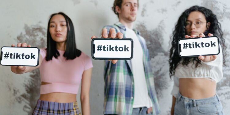 Üç genç elinde #tiktok yazılı akıllı telefonlar tutarak poz veriyor.
