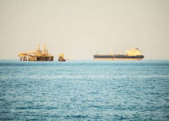 Denizde seyreden büyük bir yük gemisi ve uzaktaki petrol platformu