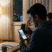 Evde akşam vakti akıllı telefonundan sosyal medyada gezinen genç bir adam.